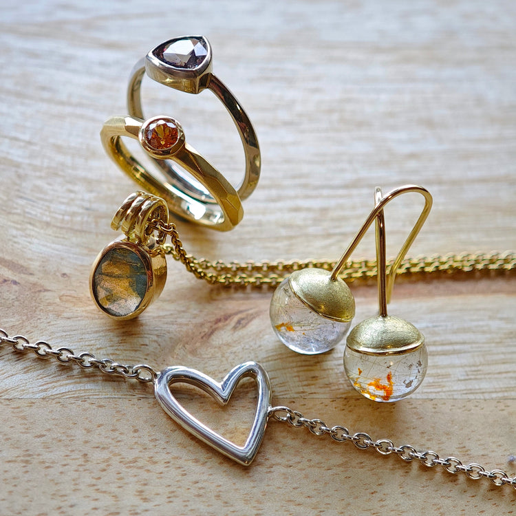 Übersicht verschiedener Schmuckstücke aus Gold und Silber mit Ringen, Ohrhängern, einer Kette und einem Armband mit Herzanhänger