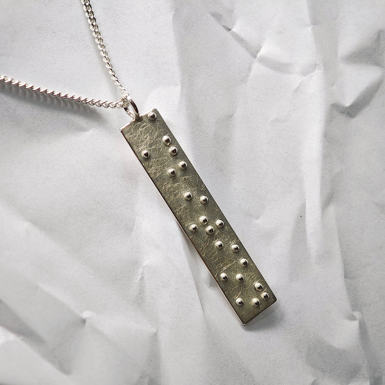 Brailleschrift, Kettenanhänger mit Blindenschrift aus massivem Silber, Nahaufnahme einer Sonderanfertigung im Kundenauftrag auf hellemm Untergrund