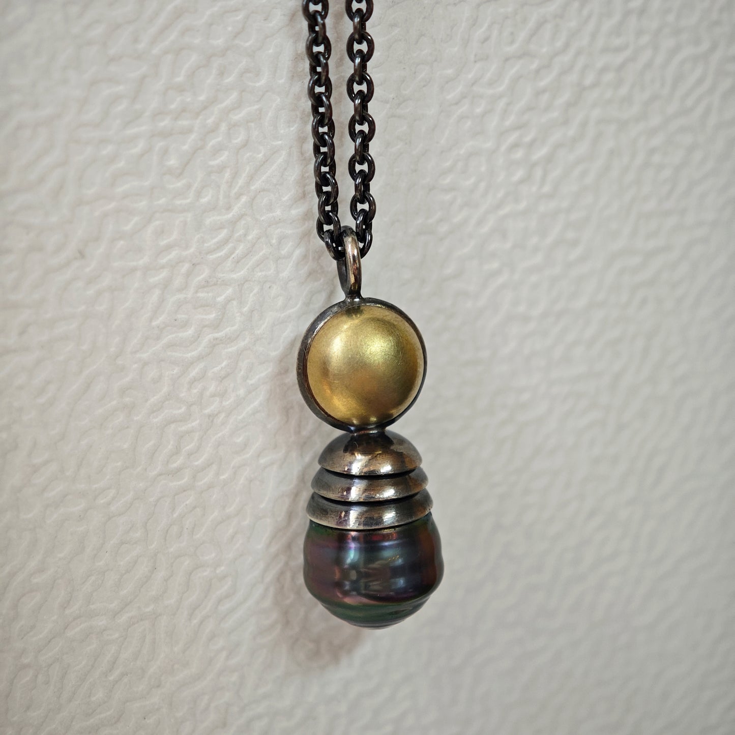 Nahaufnahme von Kettenanhänger auf hellem Untergrund: Tahiti-Perle in oxidiertem Silber und Gelbgold