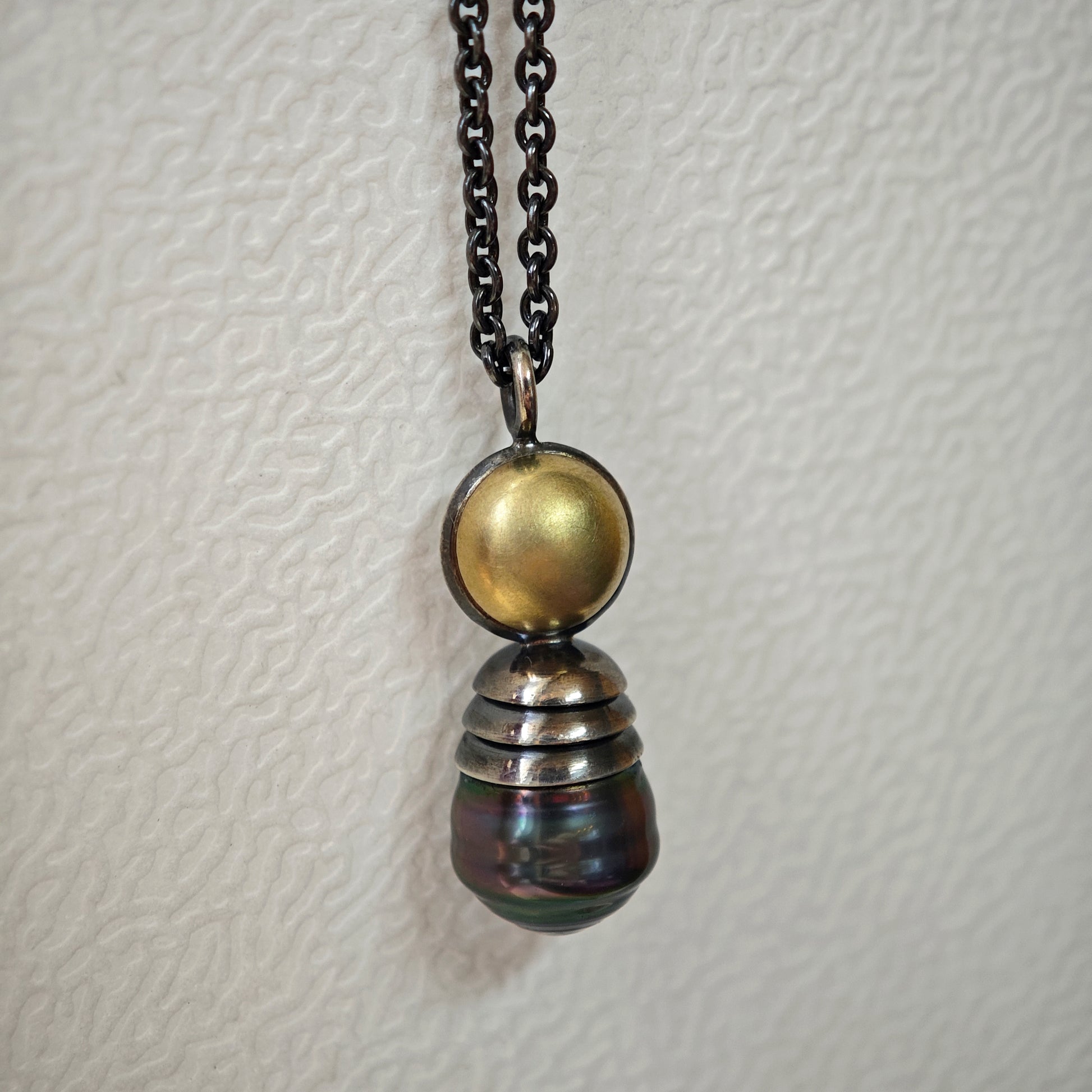 Nahaufnahme von Kettenanhänger auf hellem Untergrund: Tahiti-Perle in oxidiertem Silber und Gelbgold