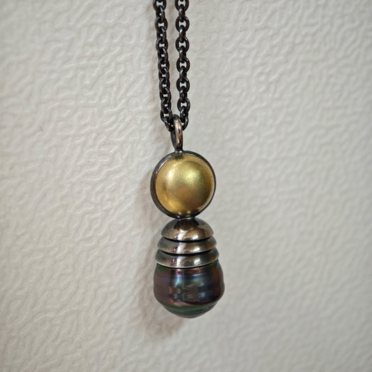 Nahaufnahme von Kettenanhänger auf hellem Untergrund: Tahiti-Perle in oxidiertem Silber und Gelbgold