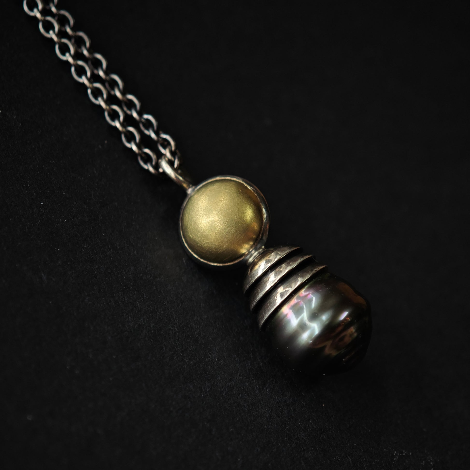 Nahaufnahme von Kettenanhänger auf dunklem Untergrund: Tahiti-Perle in oxidiertem Silber und Gold