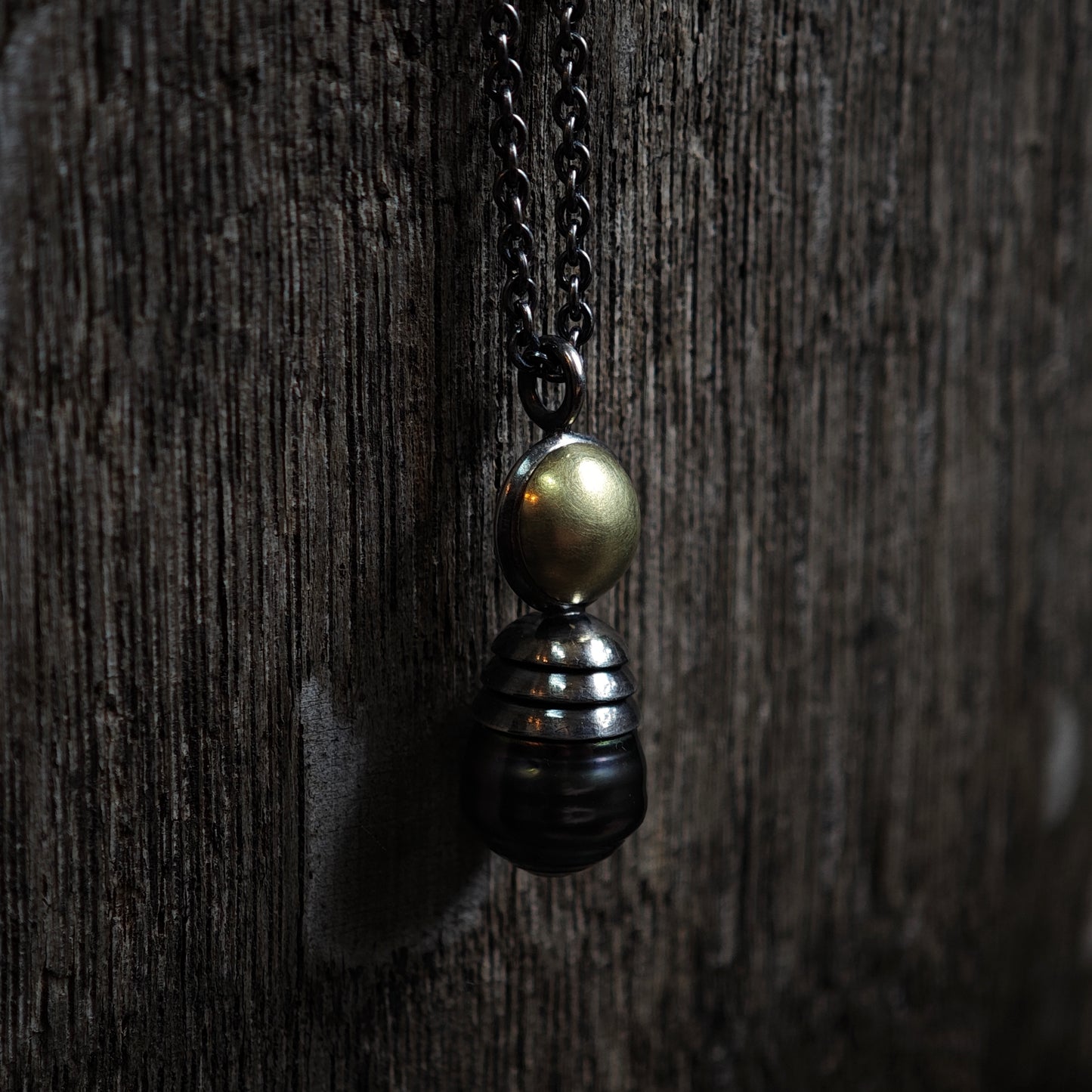 Nahaufnahme von Kettenanhänger auf dunklem Holz: Tahiti-Perle in oxidiertem Silber und Gelbgold