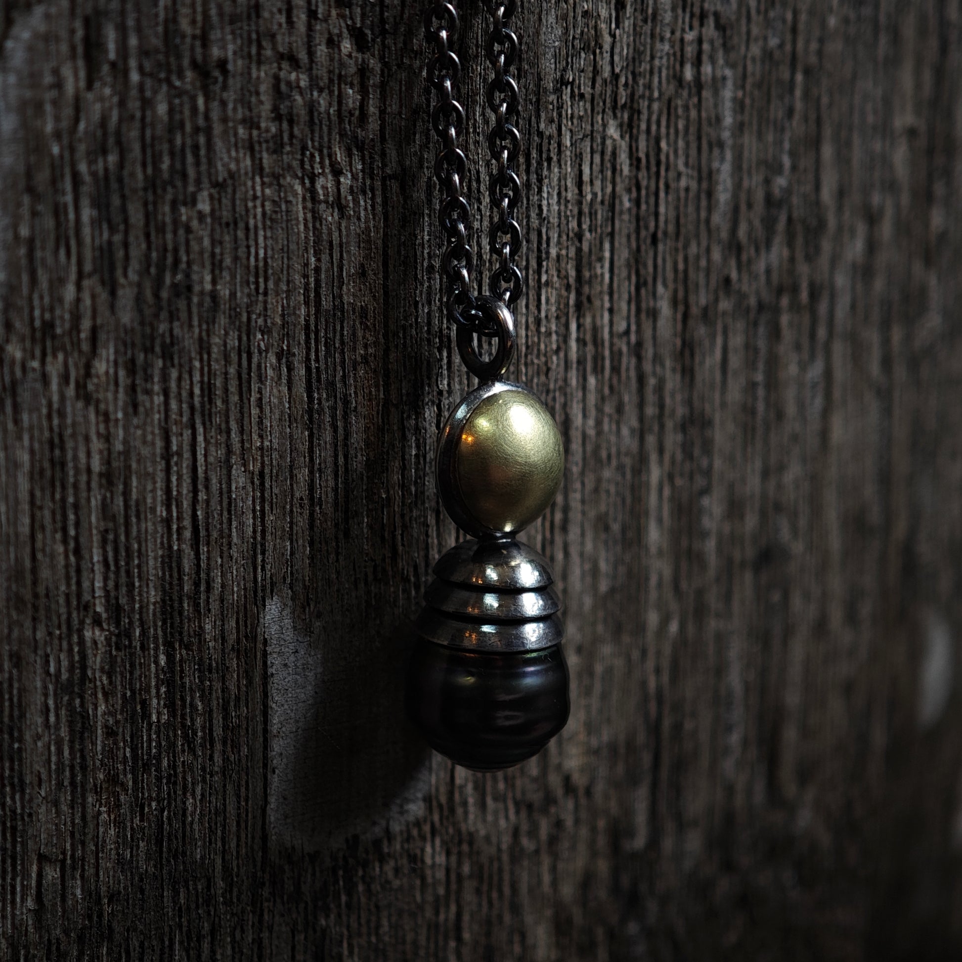 Nahaufnahme von Kettenanhänger auf dunklem Holz: Tahiti-Perle in oxidiertem Silber und Gelbgold