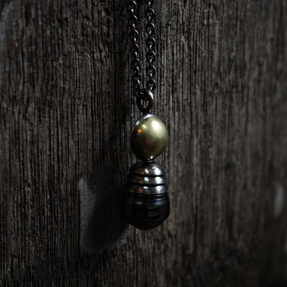 Nahaufnahme von Kettenanhänger auf dunklem Holz: Tahiti-Perle in oxidiertem Silber und Gelbgold