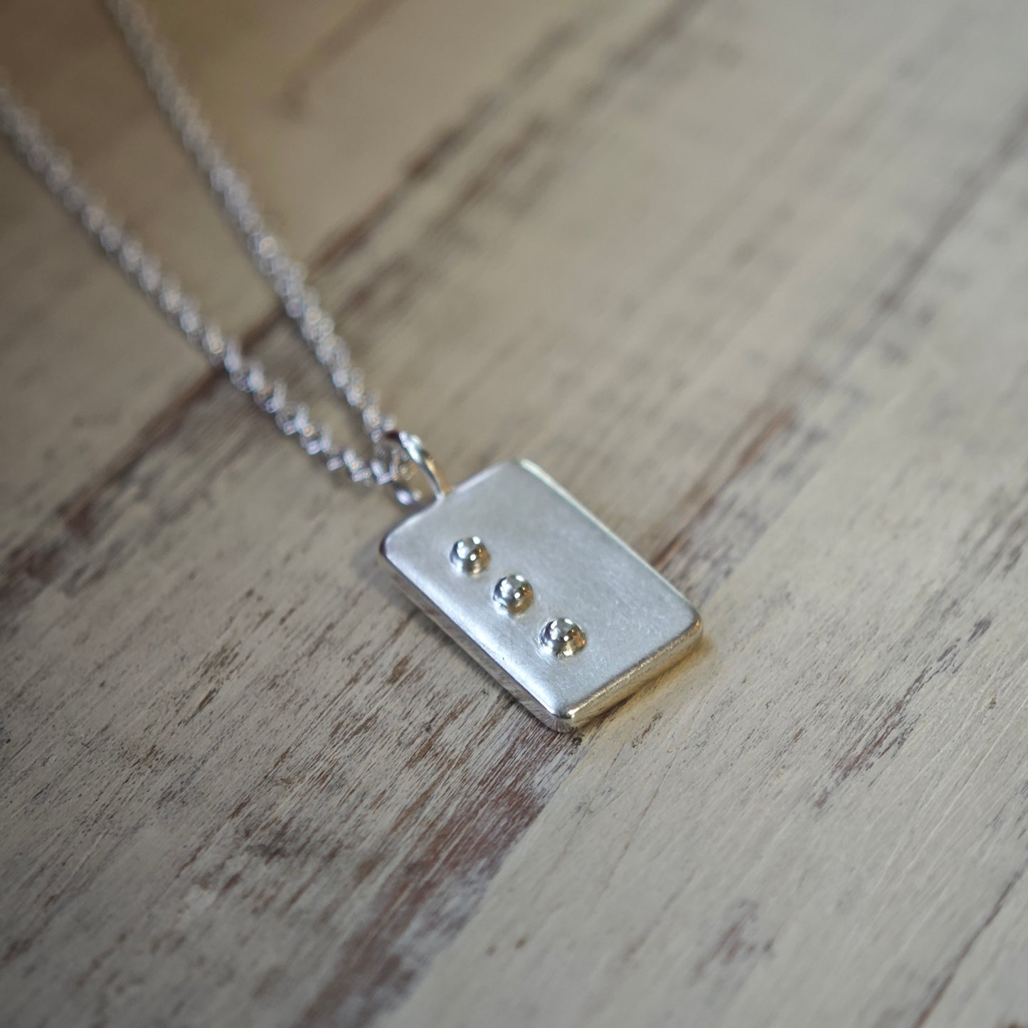 Blindenschrift-Schmuck, Nahaufnahme von Kettenanhänger mit Buchstabe in erhabener Punktschrift, lesbare Braille-Buchstaben als Kette